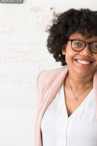 Smiling businesswoman with glasses and afro hairstyle in an office setting.